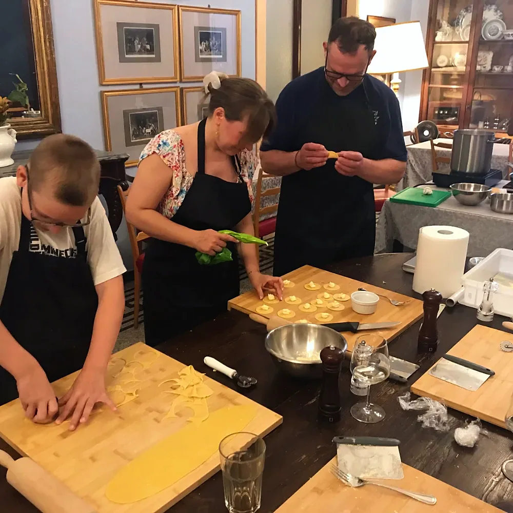 A family making fresh pasta with the chef under old portraits